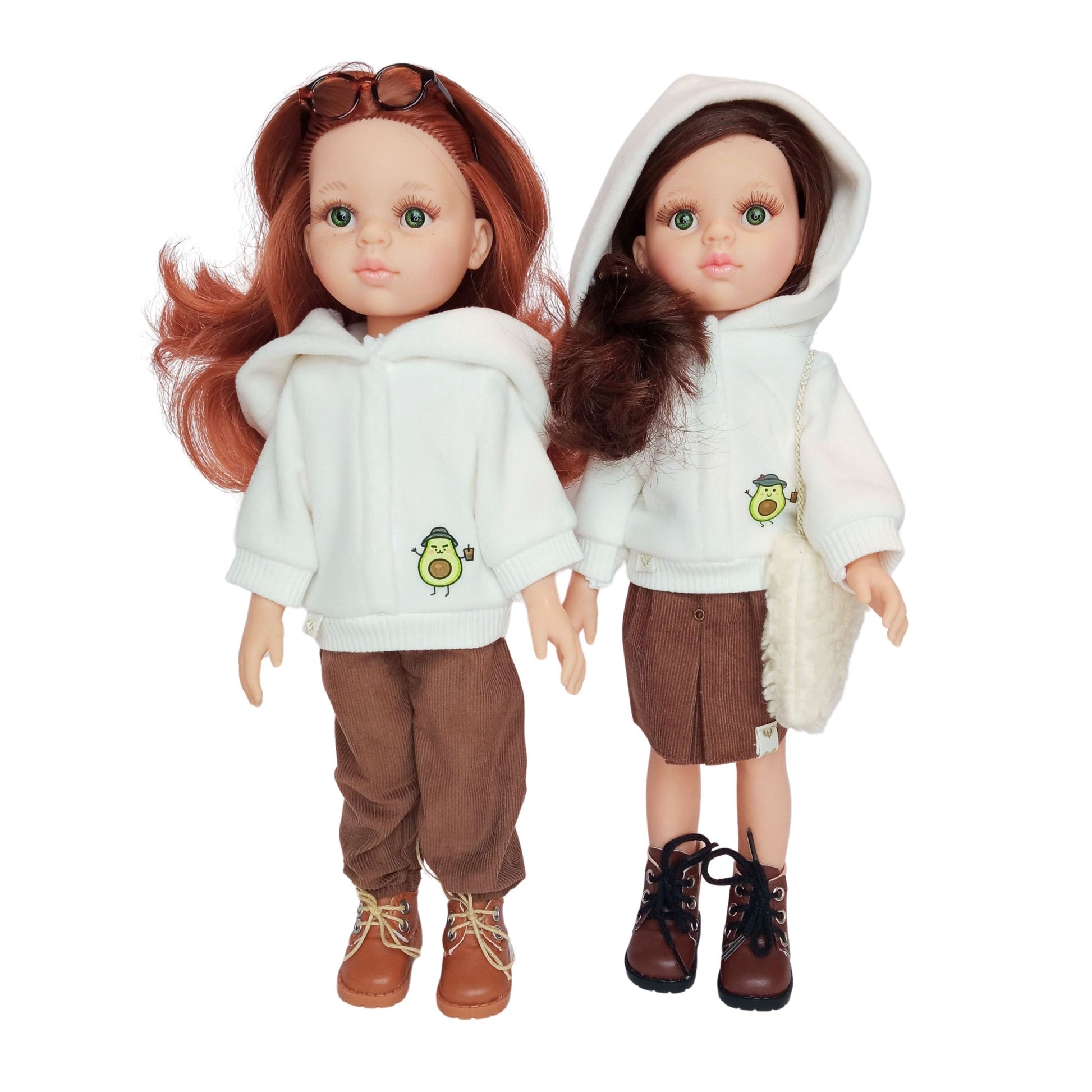 Two Paola Reina dolls wearing white hoodies with an avocado print, paired with brown corduroy pants and a skirt, styled with boots and accessories.