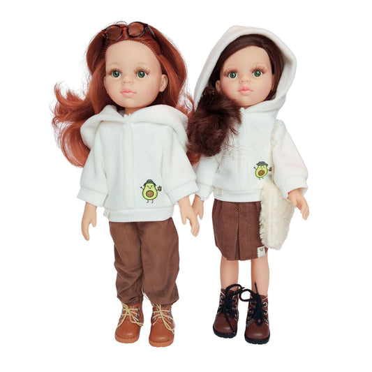 Two Paola Reina dolls wearing white hoodies with an avocado print, paired with brown corduroy pants and a skirt, styled with boots and accessories.