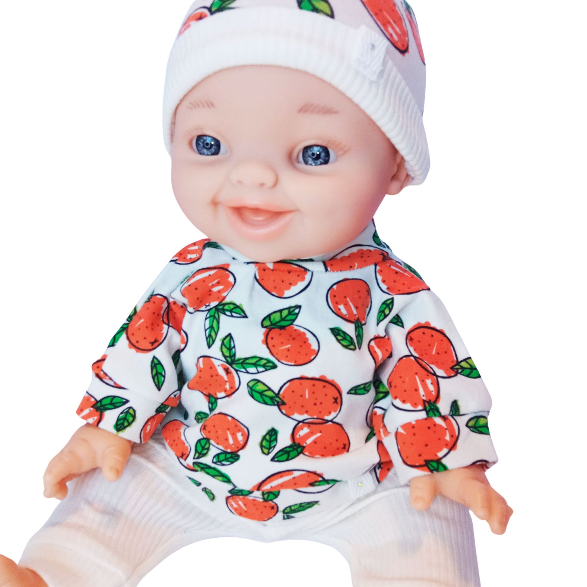 Smiling baby doll wearing a 3-piece knit outfit with orange fruit print blouse, white ribbed pants, and a matching citrus-themed hat – fits Paola Reina and Baby Born 34 cm dolls.