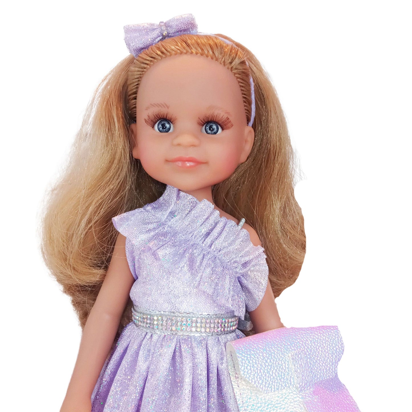 Paola Reina 32 cm doll wearing a lilac dress with ruffles, matching headband, holographic clutch.